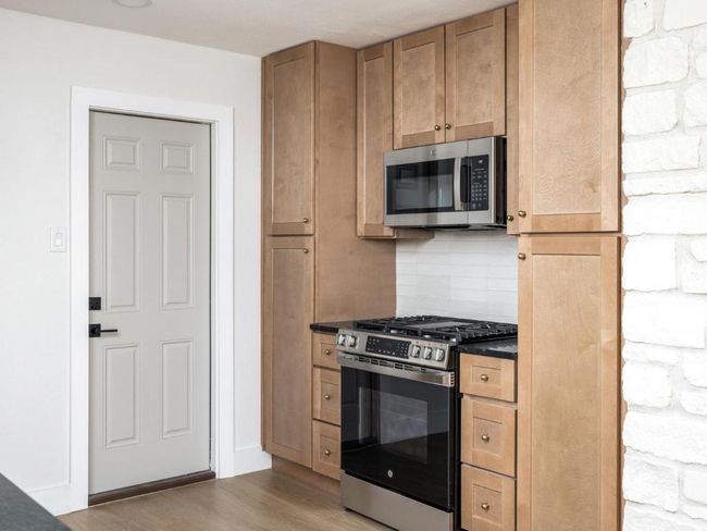 Kitchen with dark countertops, light wood-style flooring, appliances with stainless steel finishes, and tasteful backsplash | Image 16