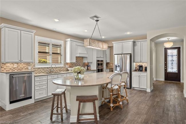 Kitchen featuring a center island, sink, stainless steel appliances, decorative light fixtures, and white cabinets | Image 8