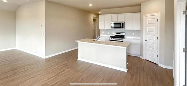 Kitchen with a center island with sink, white cabinetry, baseboards, appliances with stainless steel finishes, and wood finished floors | Image 8