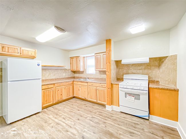 Kitchen featuring white appliances, light wood-type flooring, light brown cabinets, light countertops, and backsplash | Image 11