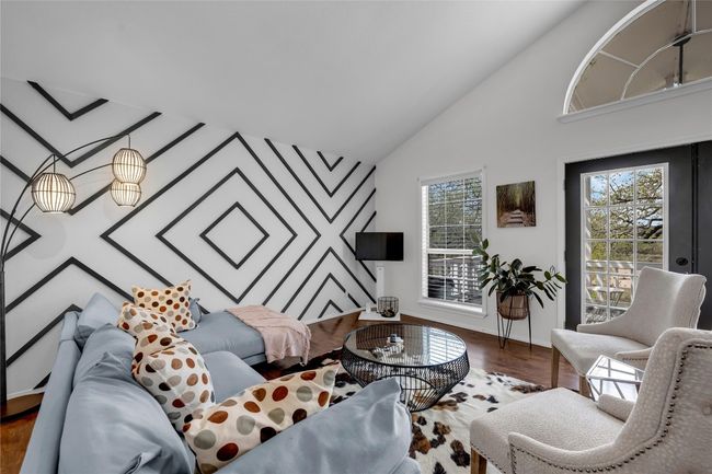 Living area featuring high vaulted ceiling, baseboards, an accent wall, and wood finished floors | Image 15