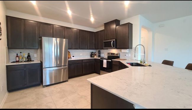 Kitchen with appliances with stainless steel finishes, dark brown cabinets, a peninsula, and decorative backsplash | Image 11
