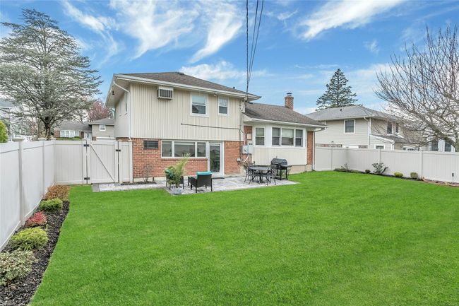 Rear view of house featuring a patio area, a lawn, a fenced backyard, brick siding, and lush landscaped property | Image 27