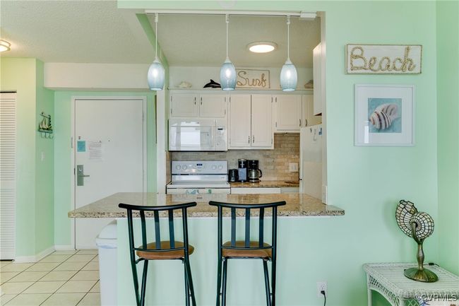Kitchen with white appliances, a peninsula, white cabinets, light tile patterned floors, and decorative backsplash | Image 7