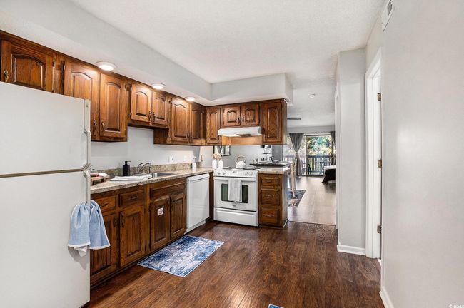 Kitchen with white appliances, dark wood-style floors, light countertops, under cabinet range hood, and brown cabinetry | Image 7