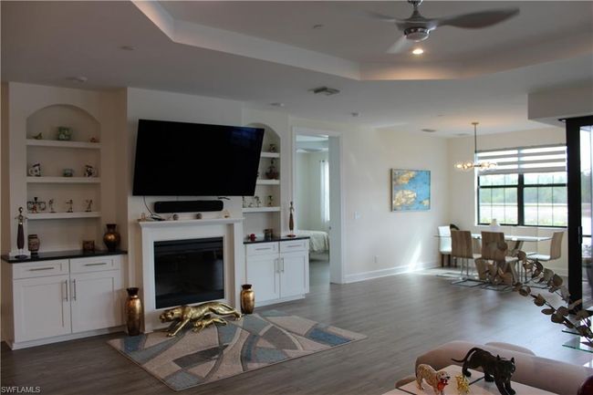 Living room featuring a glass covered fireplace, wood finished floors, a raised ceiling, built in shelves, and ceiling fan with notable chandelier | Image 8