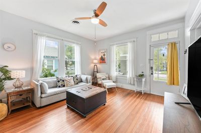 Bright and airy living room featuring hardwood floors, neutral walls, and ample natural light from multiple windows, complete with a ceiling fan and tasteful, modern decor. | Image 3