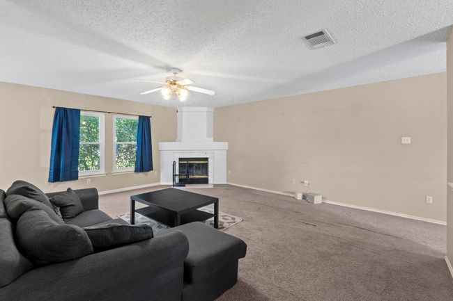 Living area featuring ceiling fan, baseboards, a textured ceiling, carpet flooring, and a premium fireplace | Image 7