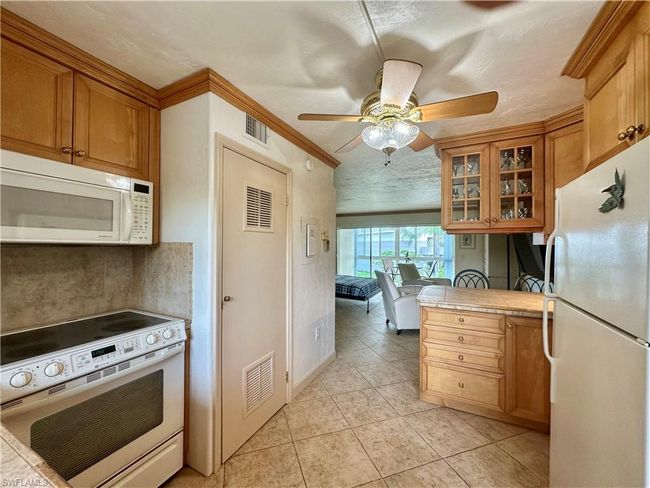 Kitchen with white appliances, tan cabinetry, glass insert cabinets, and tile countertops. New water heater | Image 12