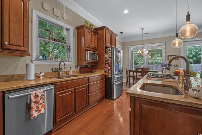 Kitchen featuring appliances with stainless steel finishes, decorative light fixtures, light stone countertops, a chandelier, and crown molding | Image 18