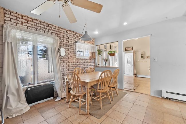 Dining room featuring a ceiling fan, brick wall, light tile patterned floors, a baseboard heating unit, and recessed lighting | Image 5
