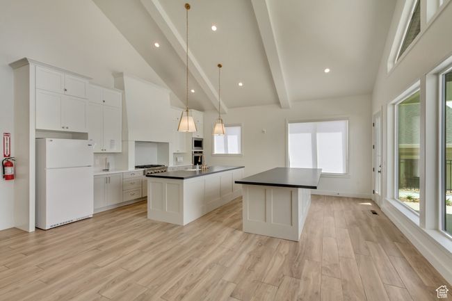 Kitchen featuring high vaulted ceiling, dark countertops, beamed ceiling, a center island with sink, and freestanding refrigerator | Image 36