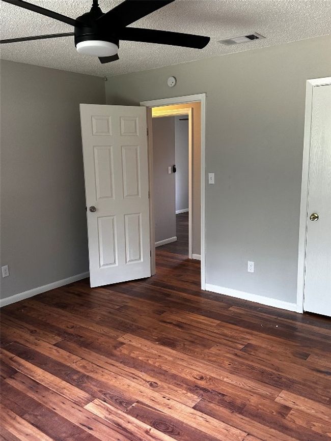 Unfurnished bedroom with a textured ceiling, dark wood-style flooring, and ceiling fan | Image 10