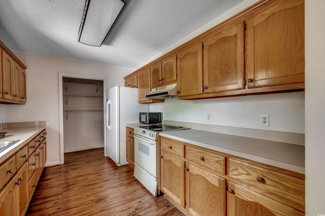Kitchen featuring electric range, black microwave, under cabinet range hood, light wood-style flooring, and light countertops | Image 23