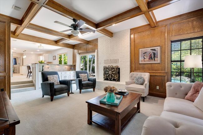 Great room featuring brick fireplace, light colored carpet, plenty of natural light, beam ceiling, and ceiling fan | Image 11