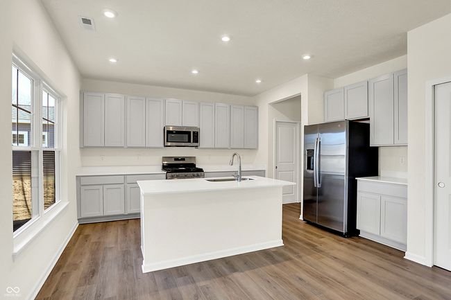 kitchen with wood finished floors, a center island with sink, a sink, stainless steel appliances, and light countertops | Image 10
