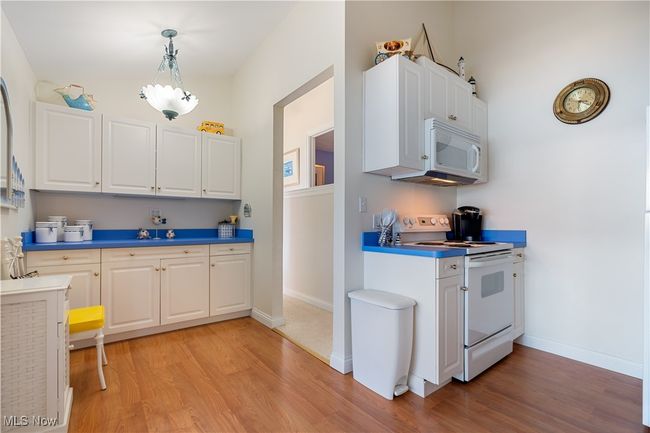 Kitchen with white appliances, light wood finished floors, white cabinets, and hanging light fixtures | Image 9