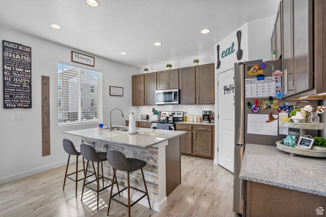 Kitchen with stainless steel appliances, backsplash, a sink, light wood-type flooring, and a kitchen bar | Image 9