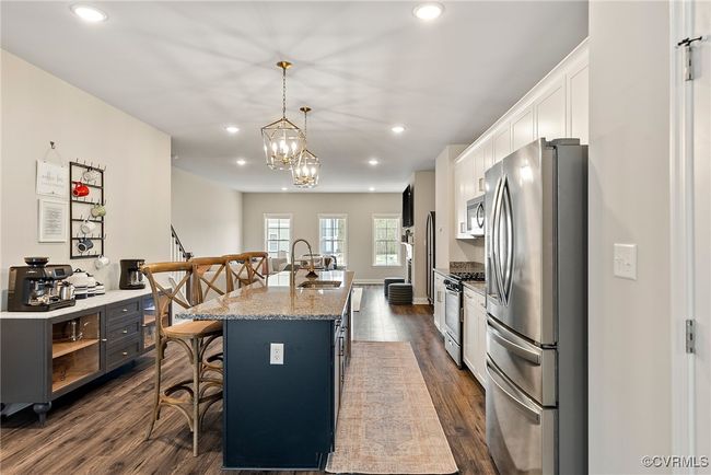Kitchen with white cabinetry, stainless steel appliances, dark hardwood / wood-style flooring, a breakfast bar area, and a center island with sink | Image 30