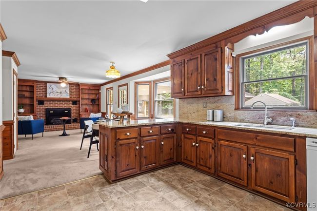 Kitchen with a fireplace, a peninsula, light stone countertops, open floor plan, and ornamental molding | Image 9