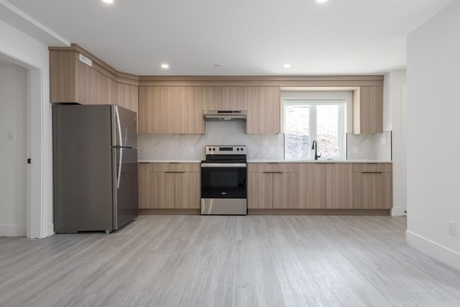 Kitchen featuring light brown cabinets, stainless steel appliances, decorative backsplash, under cabinet range hood, and modern cabinets | Image 34