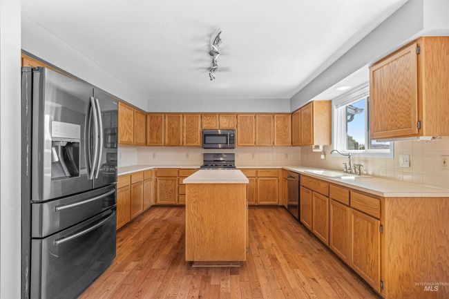 Kitchen with appliances with stainless steel finishes, a center island, light wood finished floors, light countertops, and backsplash | Image 4