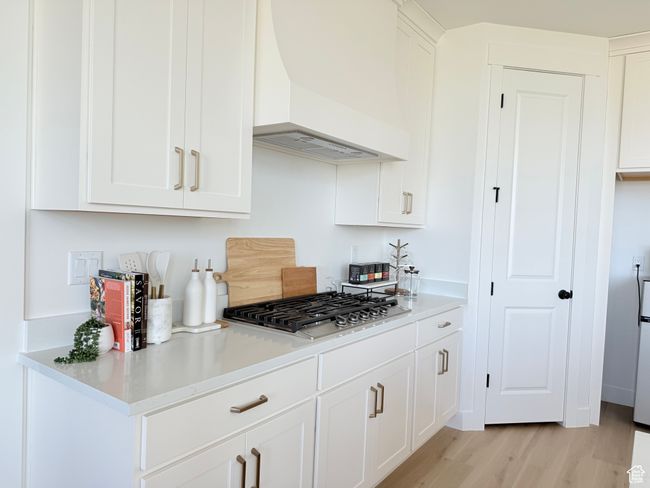 Kitchen with premium range hood, stainless steel gas stovetop, light wood-type flooring, white cabinets, and light countertops | Image 6