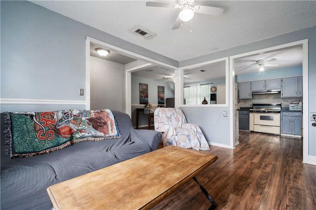 Living area featuring ceiling fan, a textured ceiling, visible vents, baseboards, and dark wood-style floors | Image 6