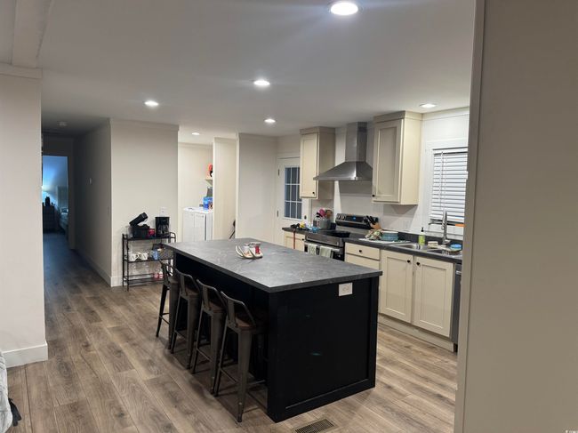Kitchen with wall chimney exhaust hood, electric stove, dark countertops, a kitchen island, and a breakfast bar | Image 4