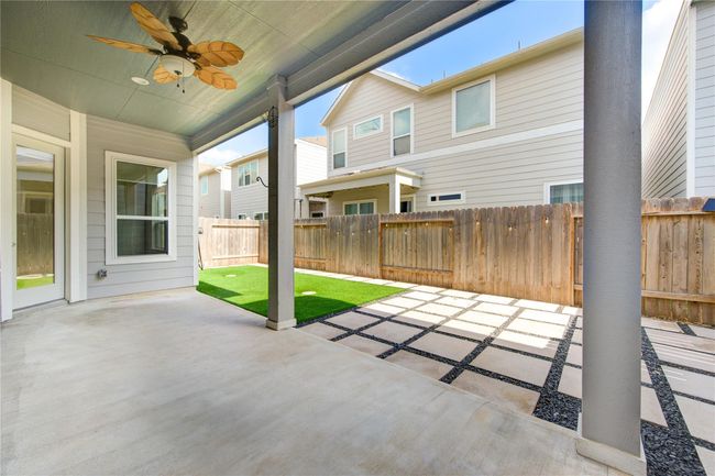 Covered patio with a ceiling fan, opening to a low-maintenance backyard featuring artificial turf and a modern paved area. | Image 34