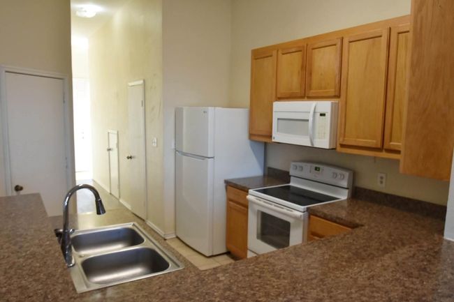 Kitchen featuring a sink, white appliances, dark countertops, and brown cabinets | Image 6
