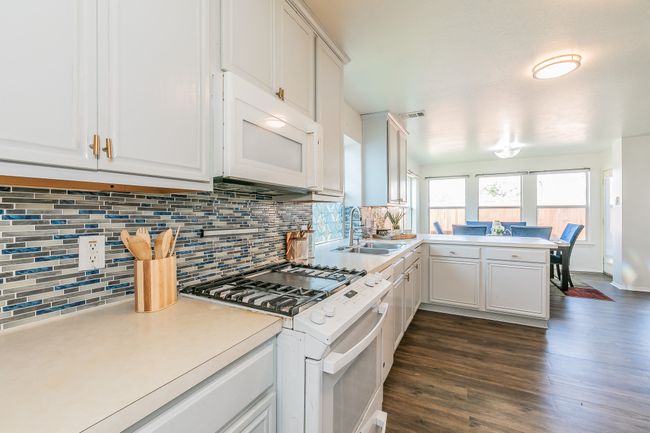 Kitchen with white appliances, a peninsula, backsplash, and dark wood-style floors | Image 4