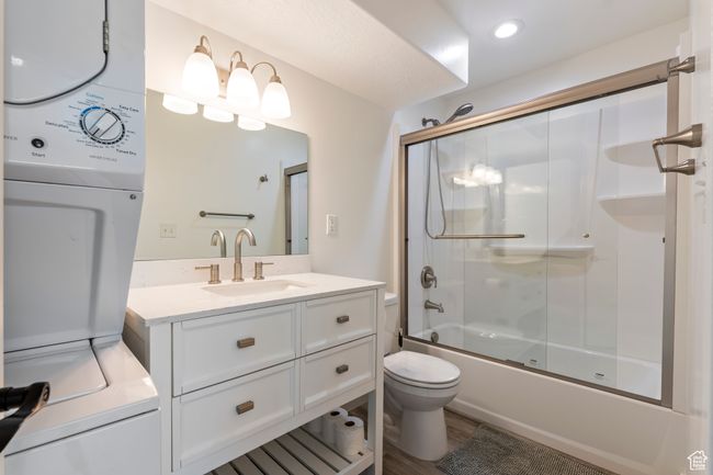 Full bathroom featuring wood finished floors, vanity, stacked washer / drying machine, enclosed tub / shower combo, and toilet | Image 33