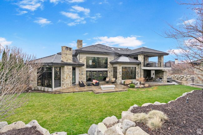 Back of house featuring a yard, stone siding, a chimney, a patio, and a balcony | Image 111