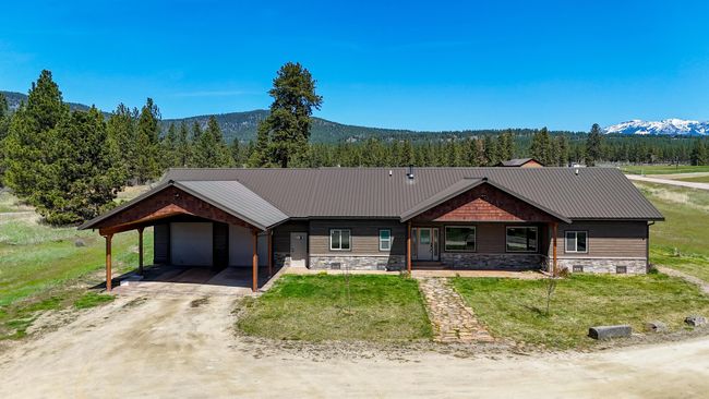 View of front of home with a carport, stone siding, a front yard, an attached garage, and a forest view | Image 22