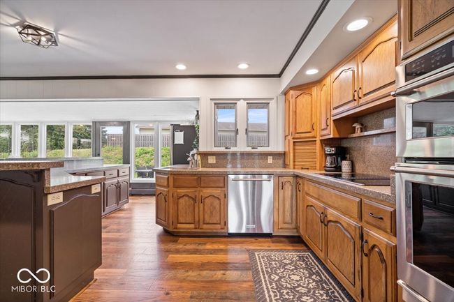 kitchen featuring appliances with stainless steel finishes, a peninsula, tasteful backsplash, dark wood-style floors, and crown molding | Image 19