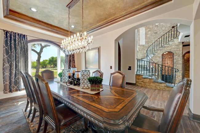 Dining space featuring crown molding, a tray ceiling, arched walkways, a chandelier, and stairs | Image 7