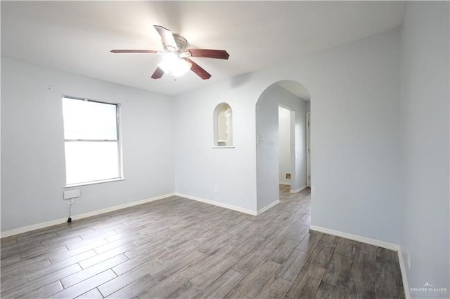 Unfurnished room featuring wood finished floors, ceiling fan, and arched walkways | Image 6