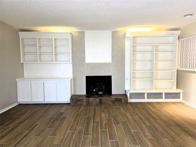 Unfurnished living room with wood finished floors, a textured ceiling, a fireplace with raised hearth, and baseboards | Image 7