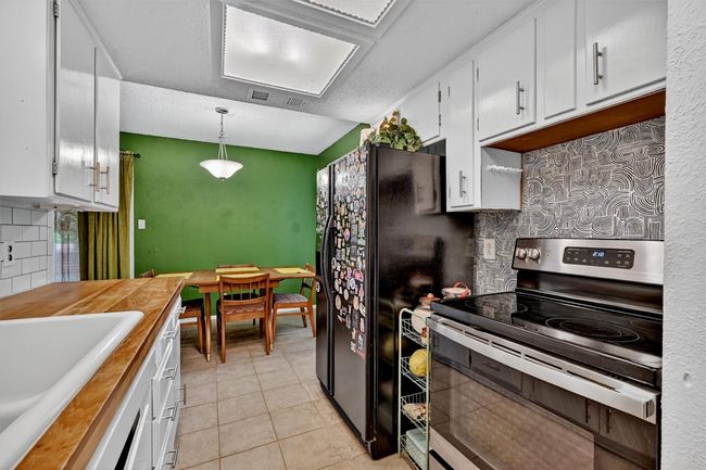 Kitchen with stainless steel electric stove, white cabinets, decorative backsplash, light tile patterned flooring, and hanging light fixtures | Image 11