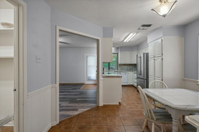Kitchen with high quality fridge, tile countertops, dishwasher, white cabinetry, and dark tile patterned floors | Image 18