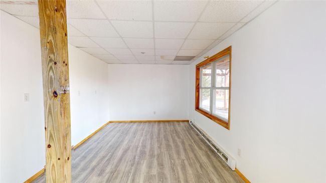 Empty room with a baseboard heating unit, wood finished floors, a paneled ceiling, and baseboards | Image 30