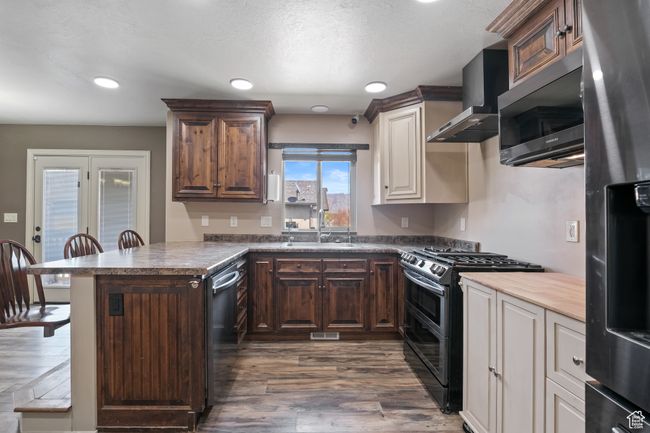 Kitchen featuring a sink, dark wood-style flooring, stainless steel appliances, wall chimney exhaust hood, and a peninsula | Image 6