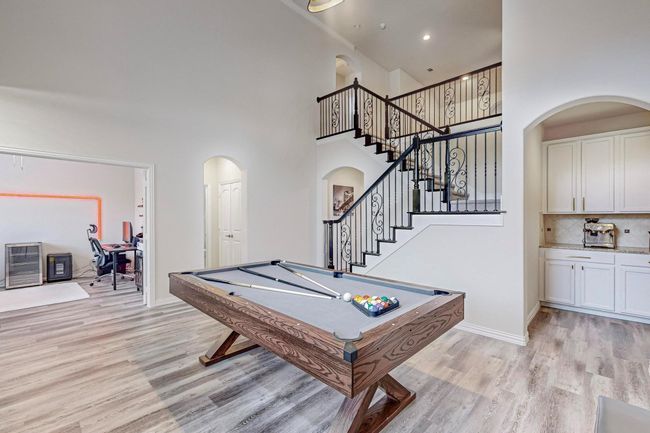 Recreation room with arched walkways, a high ceiling, light wood-style floors, pool table, and baseboards | Image 18