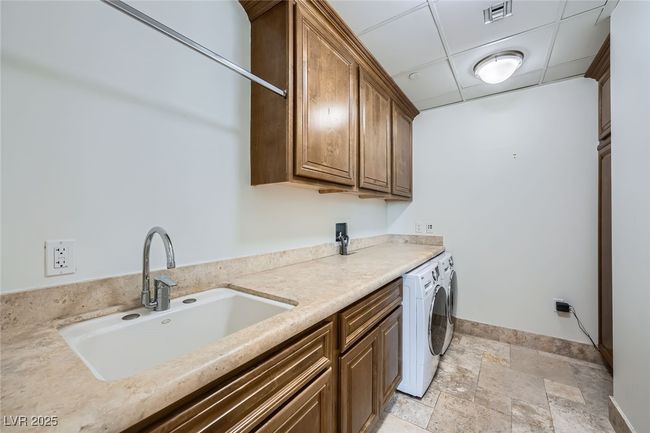 Washroom featuring cabinet space, stone tile flooring, baseboards, and washing machine and clothes dryer | Image 25