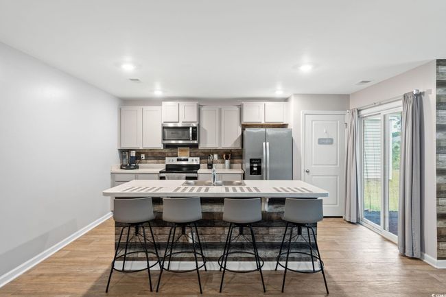 Kitchen featuring a breakfast bar area, stainless steel appliances, a center island with sink, light wood-type flooring, and white cabinetry | Image 5