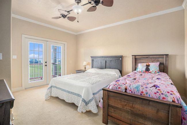 Discover another spacious secondary bedroom, large enough to comfortably fit two beds, offering exceptional versatility. French doors provide a lovely connection to the outside deck, perfect for relaxation. Crown molding adds a touch of sophisticated style to the room. | Image 25