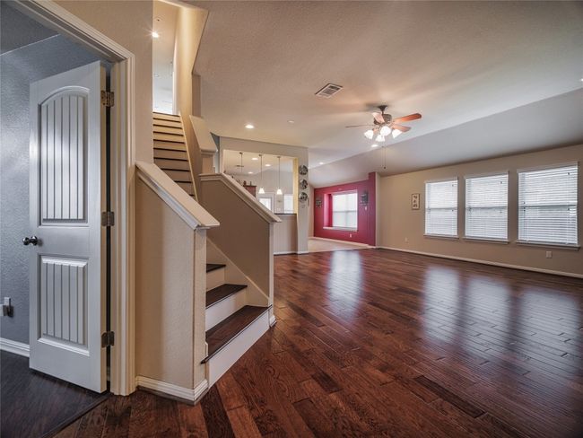 Unfurnished living room featuring a ceiling fan, dark wood-style floors, baseboards, and stairs | Image 15
