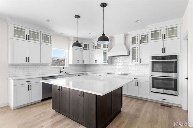 Kitchen with appliances with stainless steel finishes, custom range hood, light countertops, white cabinets, and light wood finished floors | Image 17