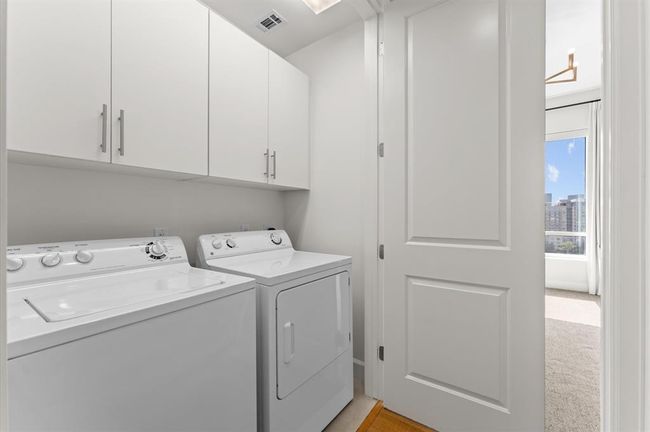 This photo shows a compact laundry room with a washing machine and dryer, white cabinetry for storage. | Image 19
